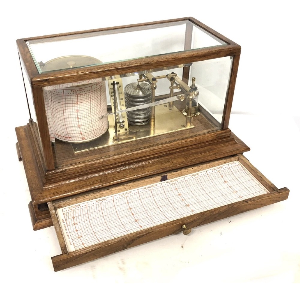 An antique oak cased barograph featuring a brass recording mechanism, internal thermometer, and bevelled glass cover over a base chart drawer. View III