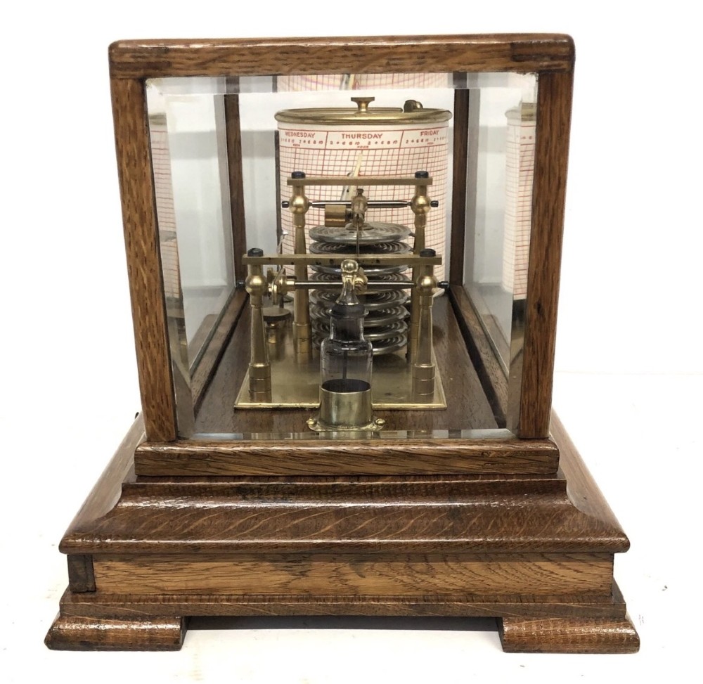 An antique oak cased barograph featuring a brass recording mechanism, internal thermometer, and bevelled glass cover over a base chart drawer. View V