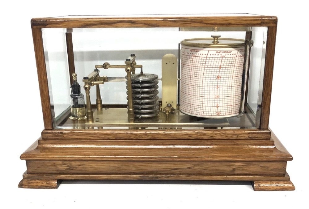 An antique oak cased barograph featuring a brass recording mechanism, internal thermometer, and bevelled glass cover over a base chart drawer. View VI