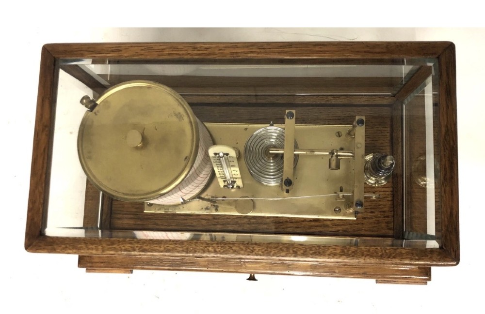 An antique oak cased barograph featuring a brass recording mechanism, internal thermometer, and bevelled glass cover over a base chart drawer. View VII