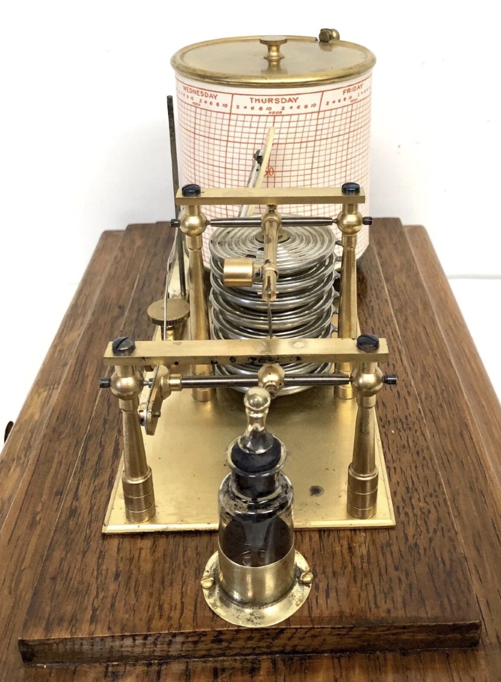 An antique oak cased barograph featuring a brass recording mechanism, internal thermometer, and bevelled glass cover over a base chart drawer. View X