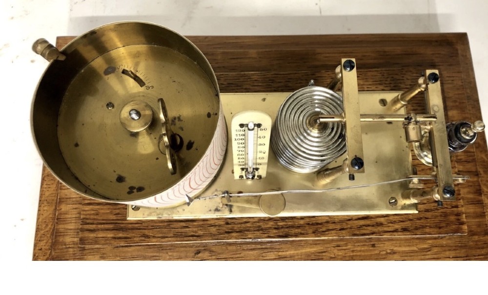 An antique oak cased barograph featuring a brass recording mechanism, internal thermometer, and bevelled glass cover over a base chart drawer. View XII