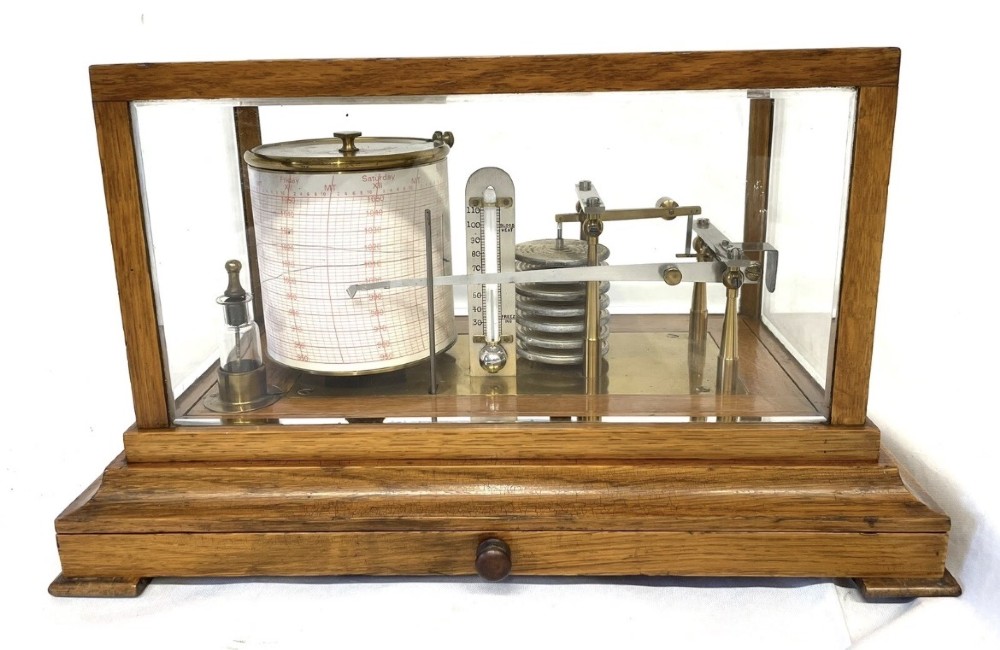 An antique barograph featuring brass recording mechanisms and a paper chart drum enclosed in a glazed oak case with a bottom chart drawer.