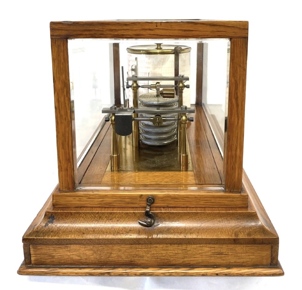 An antique barograph featuring brass recording mechanisms and a paper chart drum enclosed in a glazed oak case with a bottom chart drawer. View VI