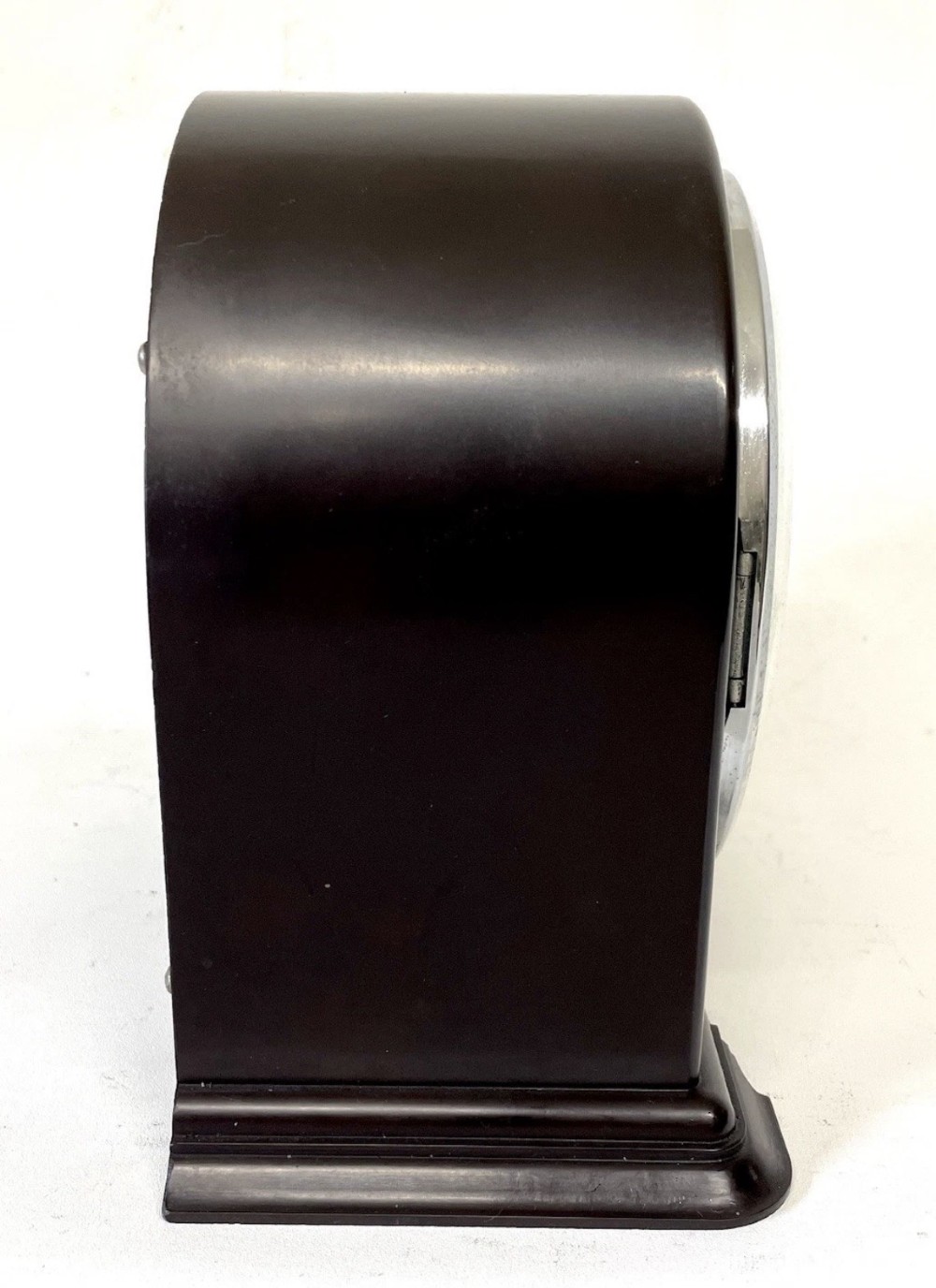 A dark brown domed Bakelite mantel clock with a round cream dial, black Arabic numerals, spade hands, and a broad arrow symbol. View VII