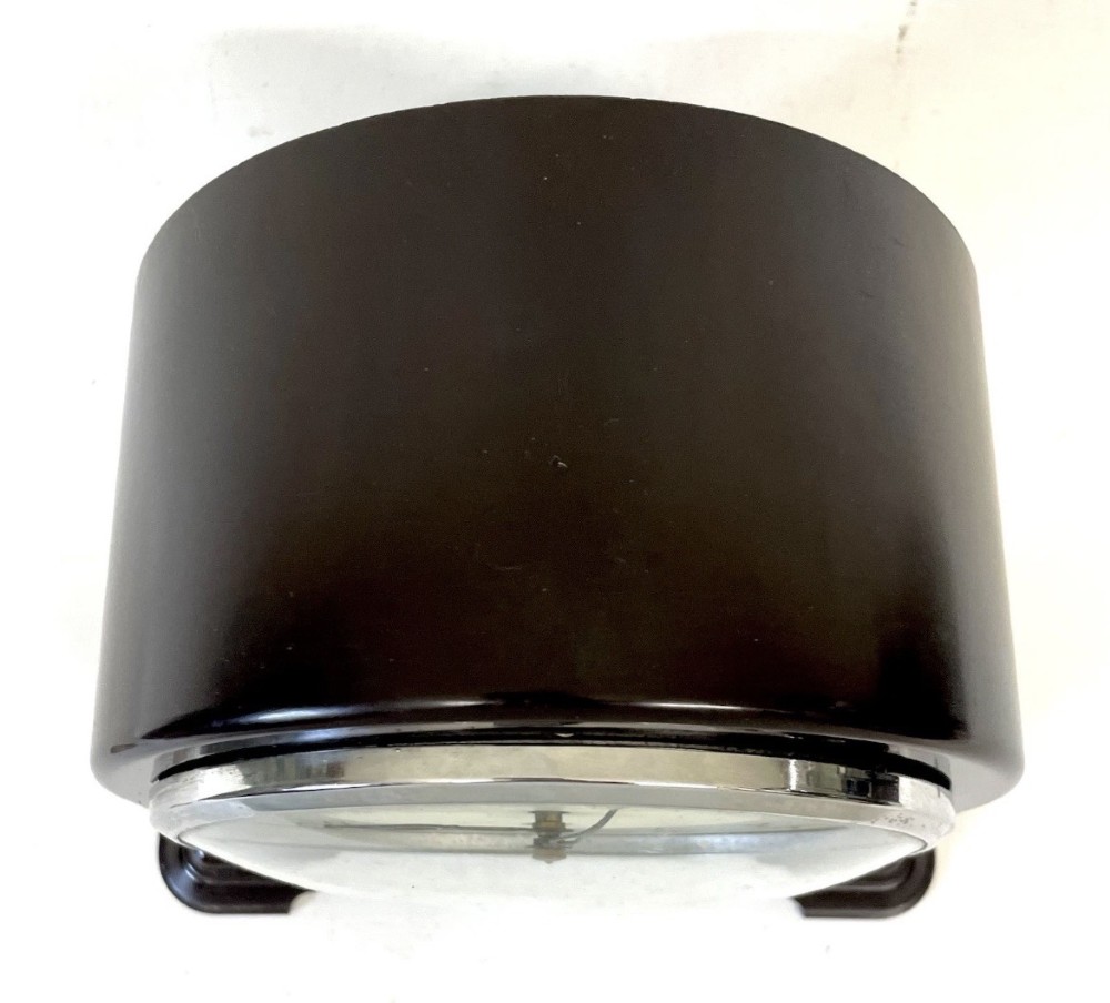 A dark brown domed Bakelite mantel clock with a round cream dial, black Arabic numerals, spade hands, and a broad arrow symbol. View VIII