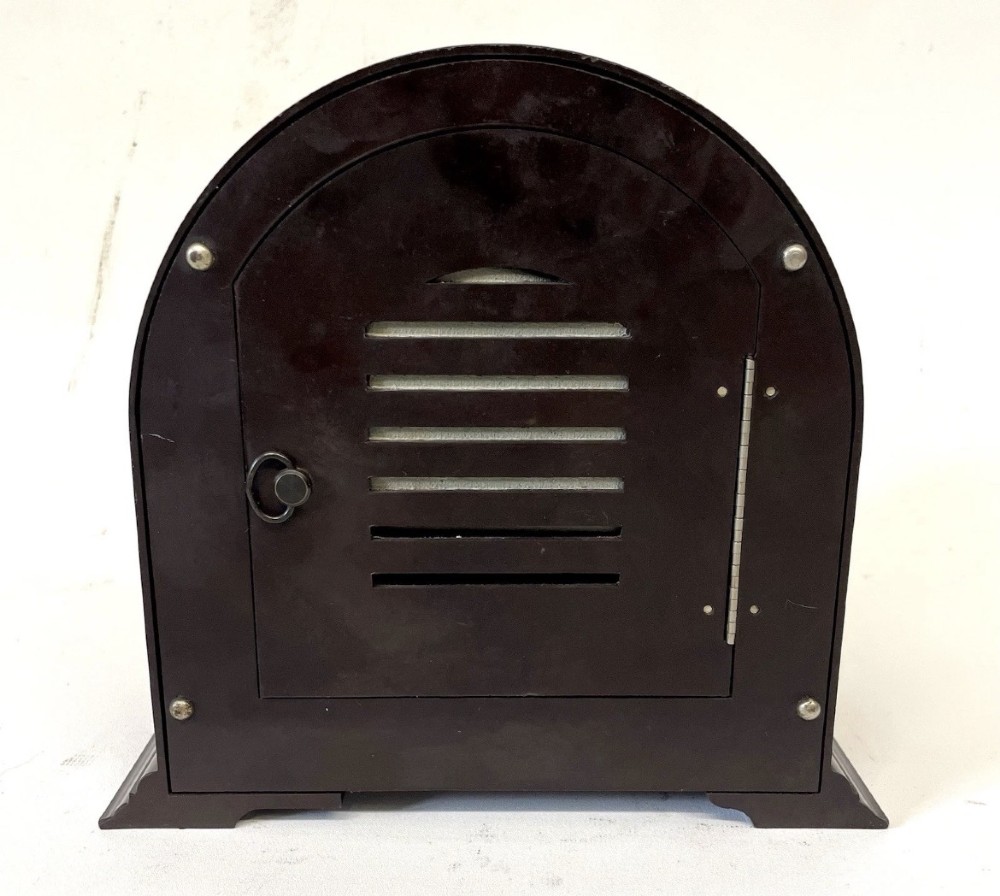 A dark brown domed Bakelite mantel clock with a round cream dial, black Arabic numerals, spade hands, and a broad arrow symbol. View X