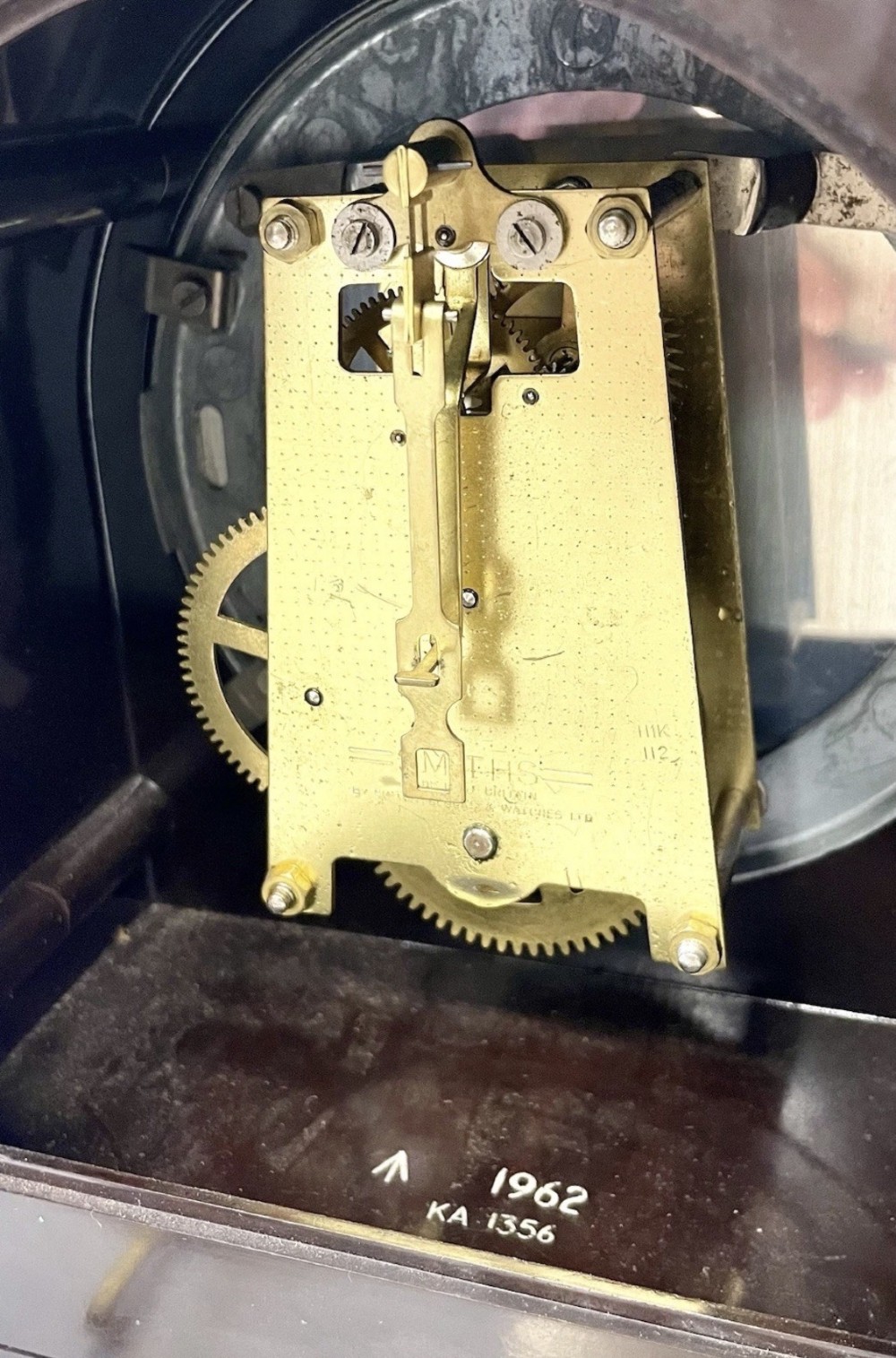A dark brown domed Bakelite mantel clock with a round cream dial, black Arabic numerals, spade hands, and a broad arrow symbol. View XII