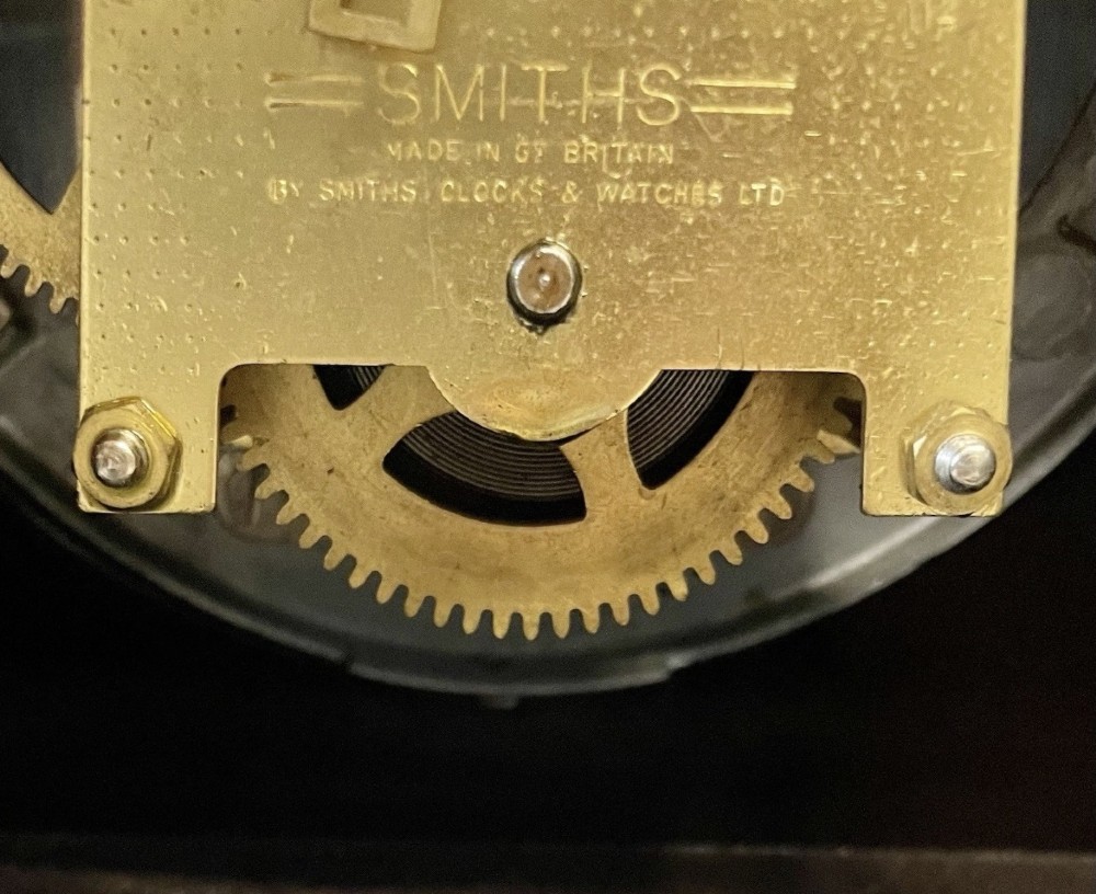 A dark brown domed Bakelite mantel clock with a round cream dial, black Arabic numerals, spade hands, and a broad arrow symbol. View XIV