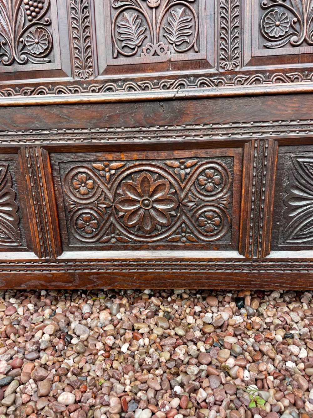 A dark carved oak box settle featuring relief floral panels on the backrest, curved armrests, and a lift-up storage seat. View IX