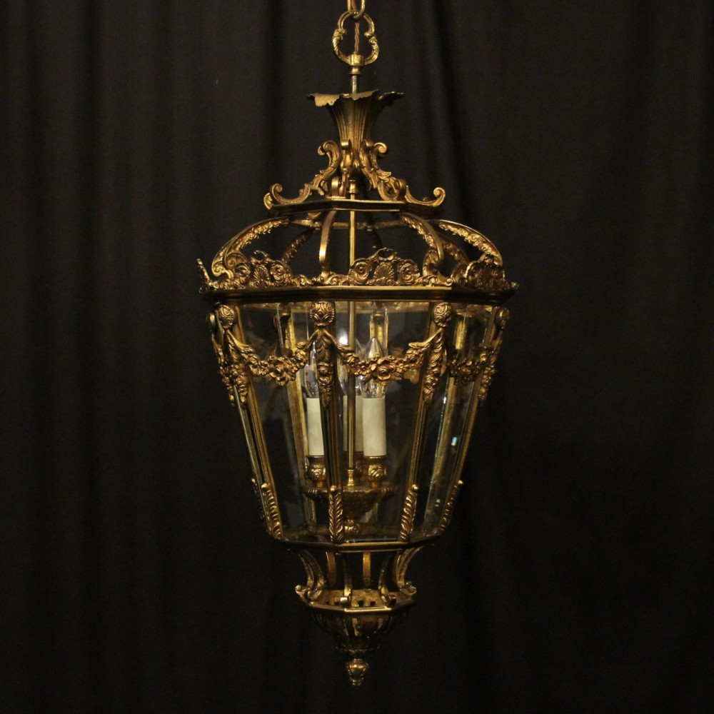 A French gilt bronze hall lantern featuring curved glass panels, ornate scrollwork cresting, and three central light fittings.