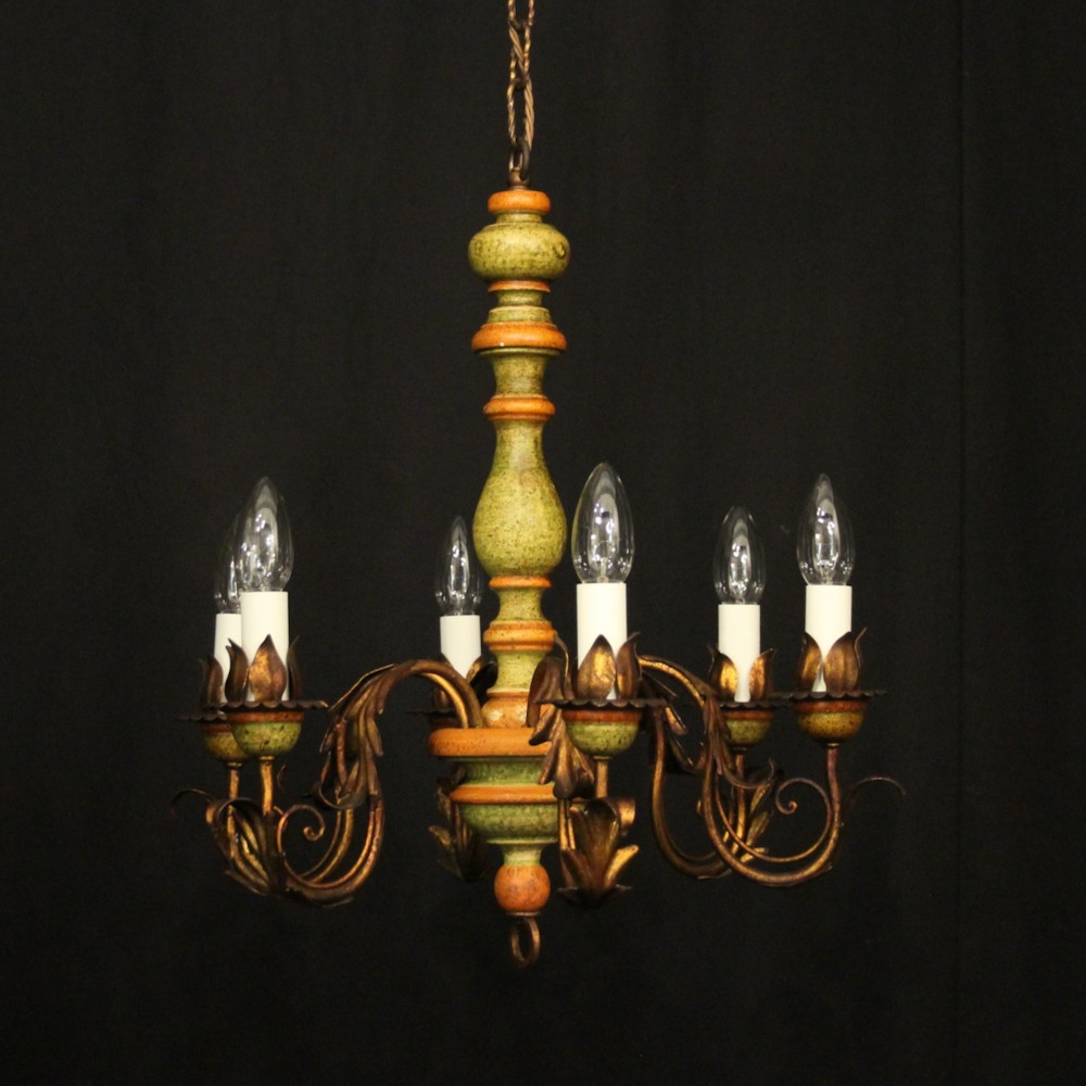 A six-arm Florentine chandelier featuring a turned wooden central stem painted in distressed green and terracotta tones with gilded leaf-adorned metal arms.