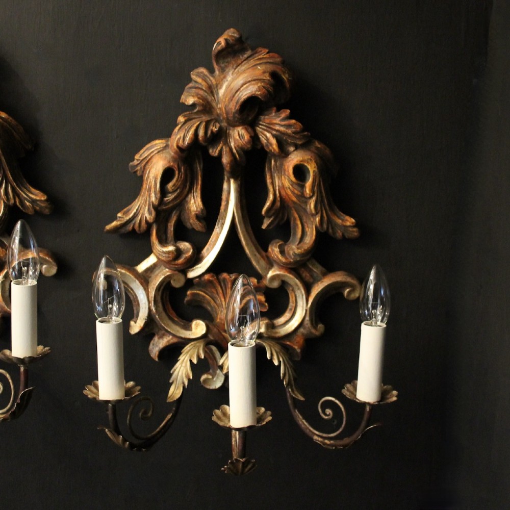 A pair of carved giltwood three-arm Florentine wall lights with ornate acanthus leaf scrollwork and candle sleeves. View II