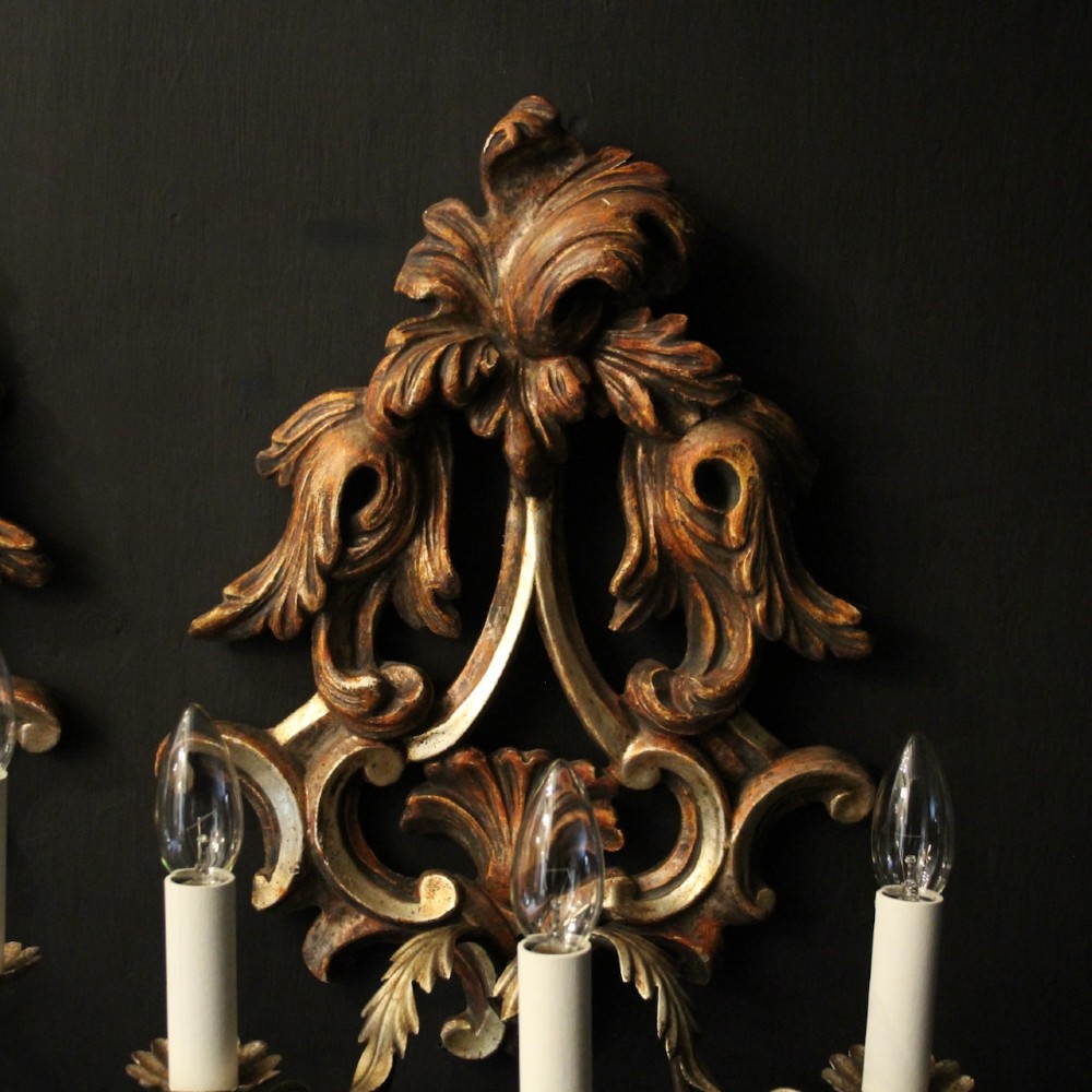 A pair of carved giltwood three-arm Florentine wall lights with ornate acanthus leaf scrollwork and candle sleeves. View IV