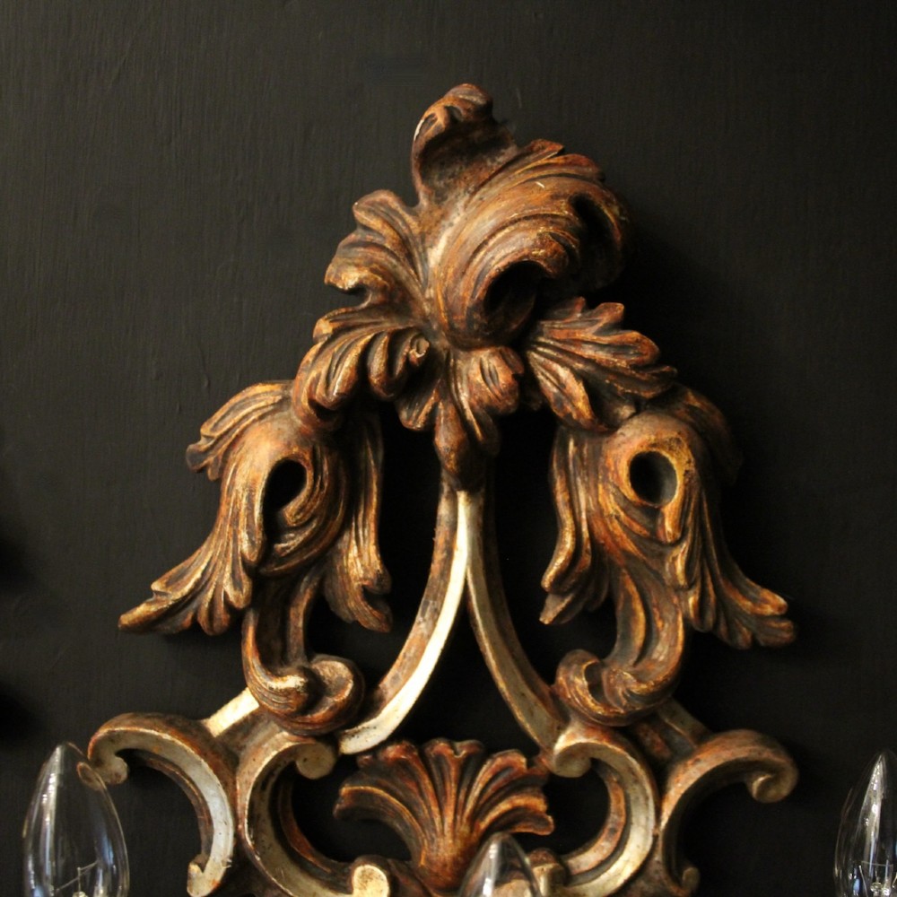 A pair of carved giltwood three-arm Florentine wall lights with ornate acanthus leaf scrollwork and candle sleeves. View V