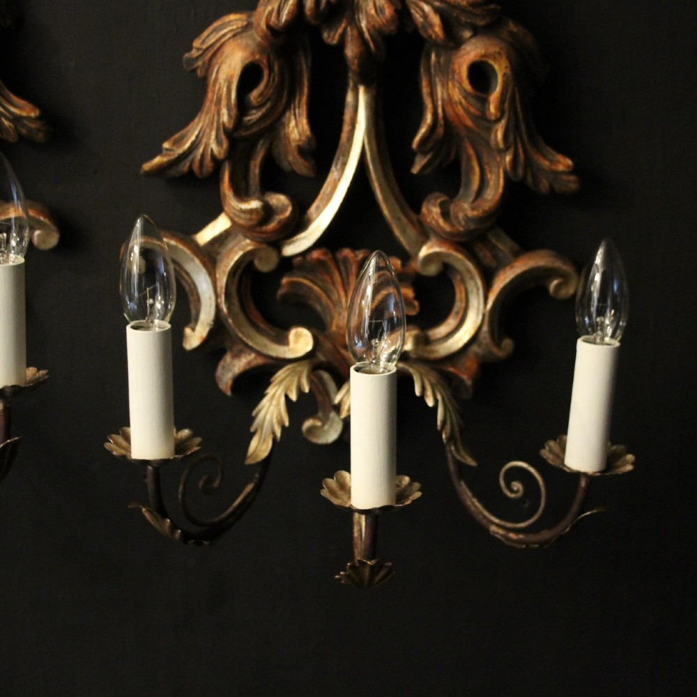 A pair of carved giltwood three-arm Florentine wall lights with ornate acanthus leaf scrollwork and candle sleeves. View IX