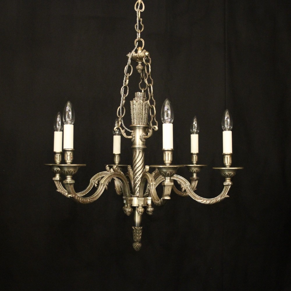 A six-arm French silver-gilded bronze chandelier featuring decorative fluted central columns, carved foliage motifs, and faux candle sleeves against a dark background.