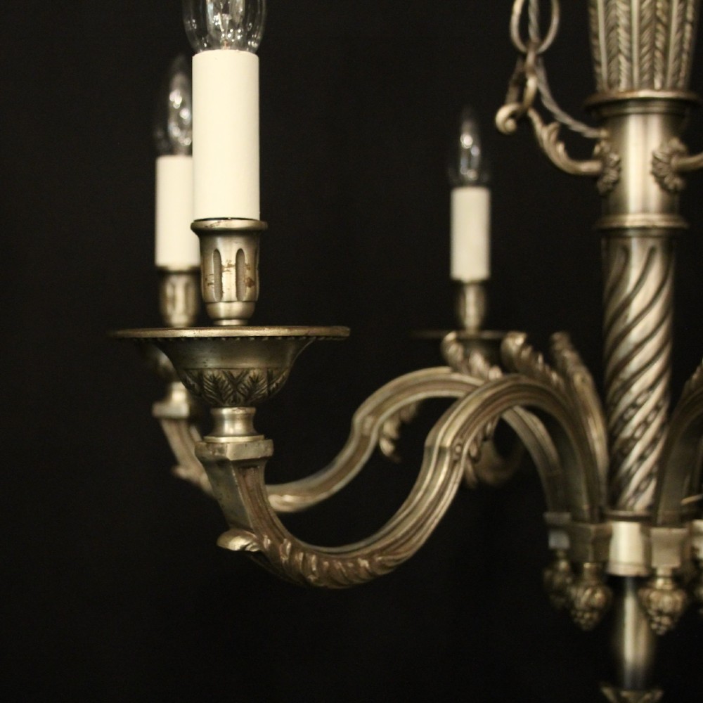 A six-arm French silver-gilded bronze chandelier featuring decorative fluted central columns, carved foliage motifs, and faux candle sleeves against a dark background. View V