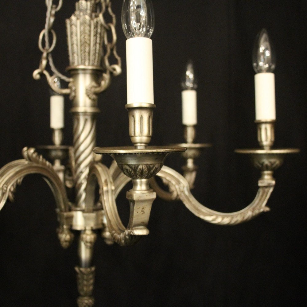 A six-arm French silver-gilded bronze chandelier featuring decorative fluted central columns, carved foliage motifs, and faux candle sleeves against a dark background. View VI