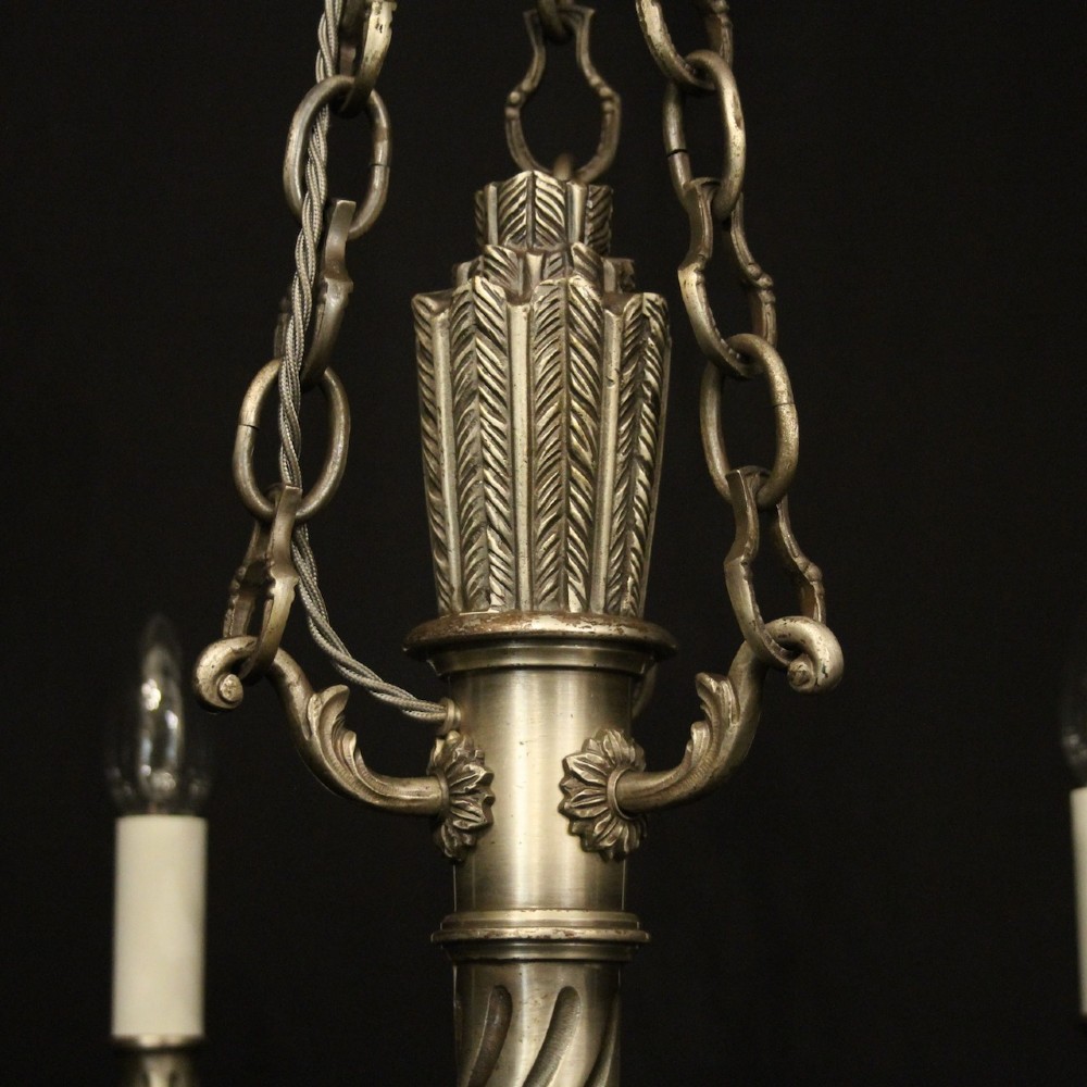 A six-arm French silver-gilded bronze chandelier featuring decorative fluted central columns, carved foliage motifs, and faux candle sleeves against a dark background. View IX