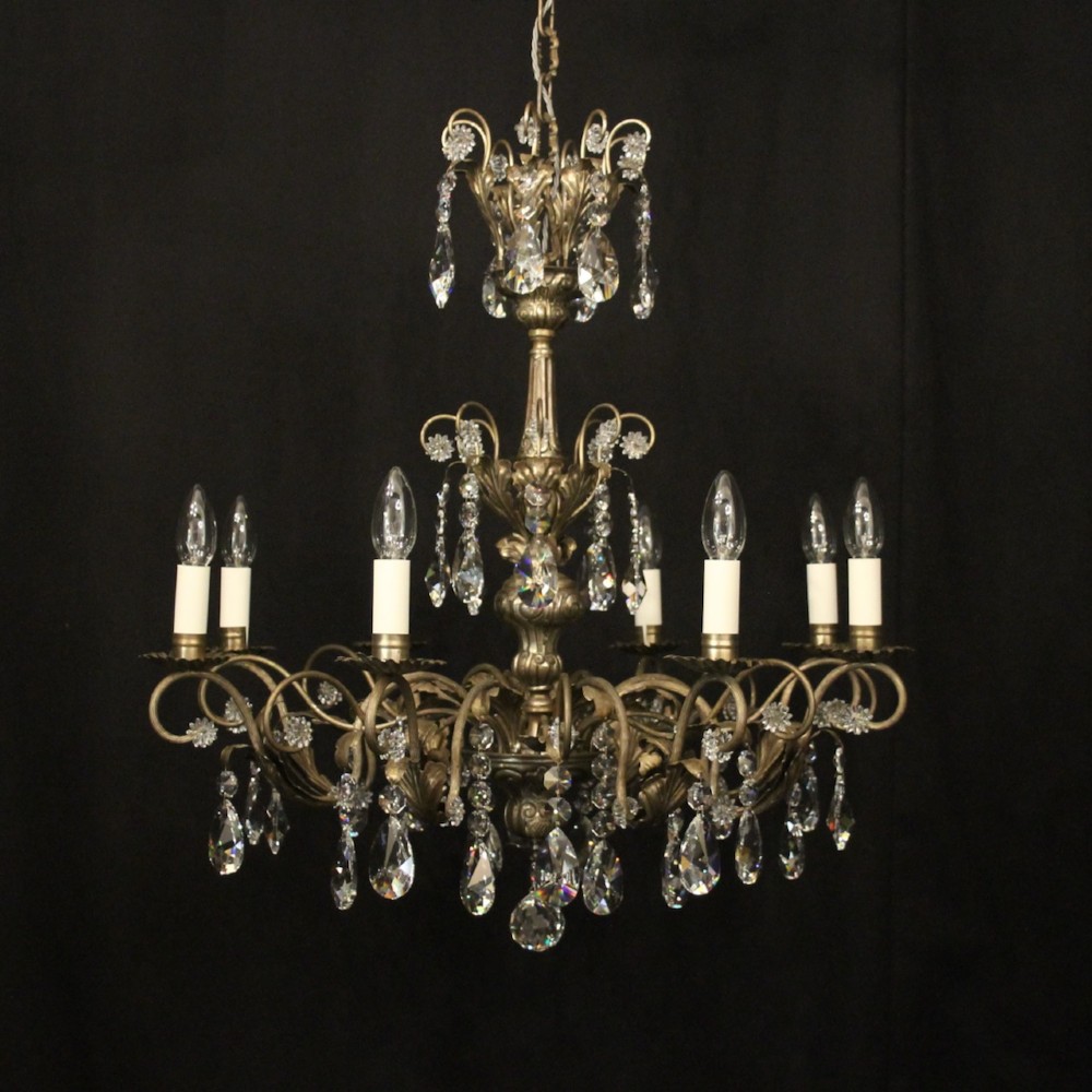 An eight-light Italian chandelier featuring a silvered metal frame decorated with scrolling arms, hanging crystal drops, and glass rosettes.