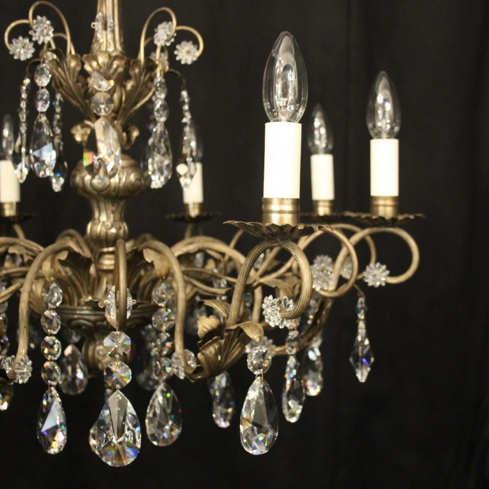 An eight-light Italian chandelier featuring a silvered metal frame decorated with scrolling arms, hanging crystal drops, and glass rosettes. View IV
