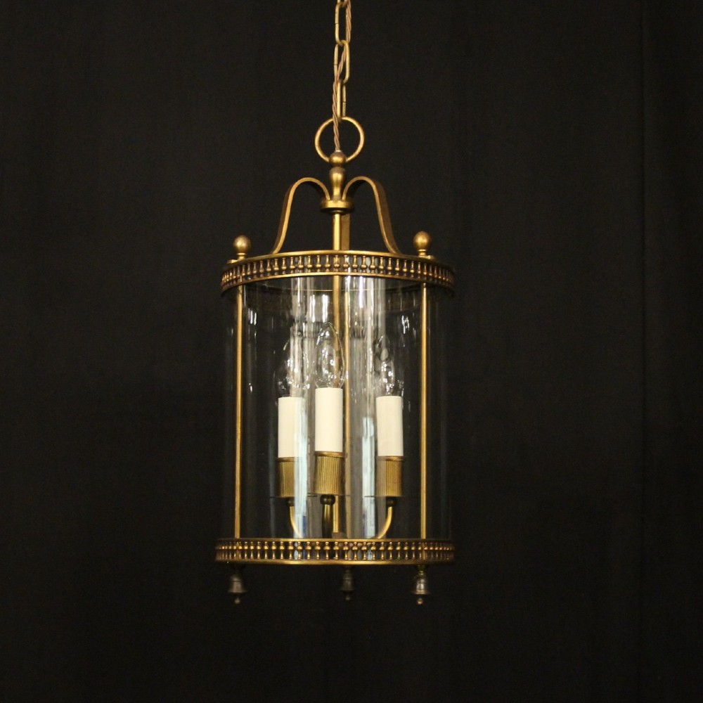 A cylindrical antique French hall lantern crafted from gilded brass with clear glass panels housing a three-light candle cluster.