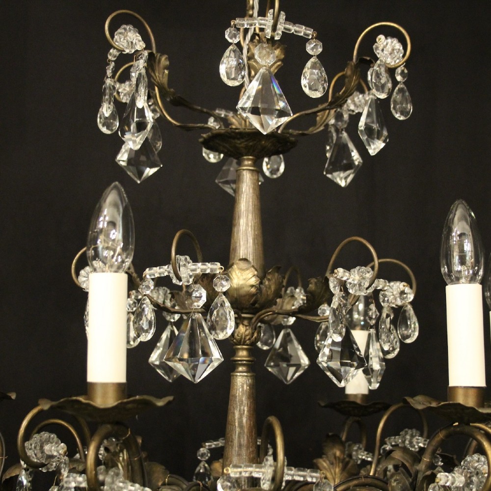 An Italian multi-tiered chandelier featuring a patinated silvered frame adorned with hanging cut-crystal drops, faceted pendants, and six candle-effect light fittings. View IX