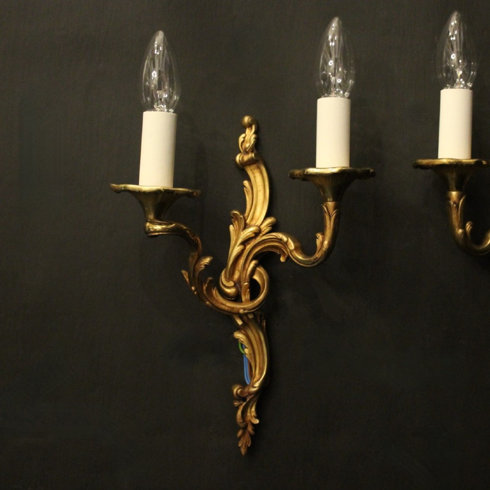A pair of two-arm French Rococo style gilded bronze wall lights featuring acanthus leaf scrollwork and cream candle holders. View II