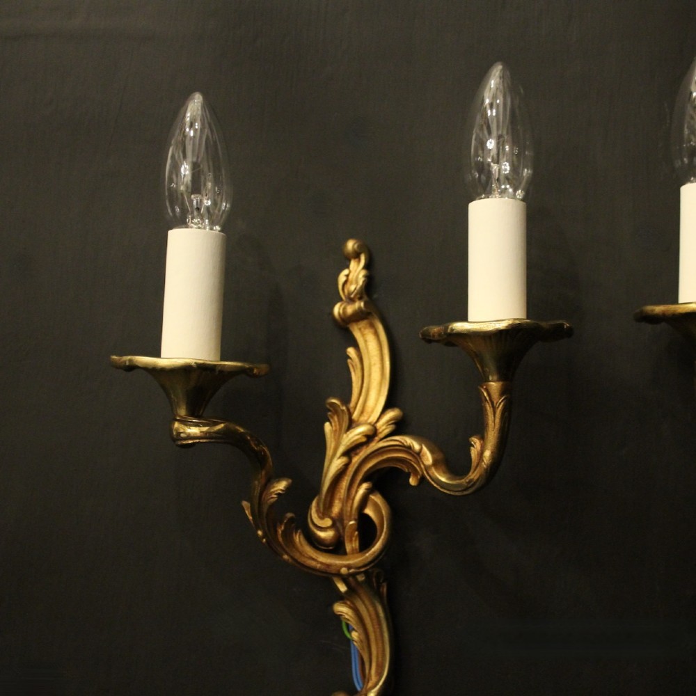 A pair of two-arm French Rococo style gilded bronze wall lights featuring acanthus leaf scrollwork and cream candle holders. View III