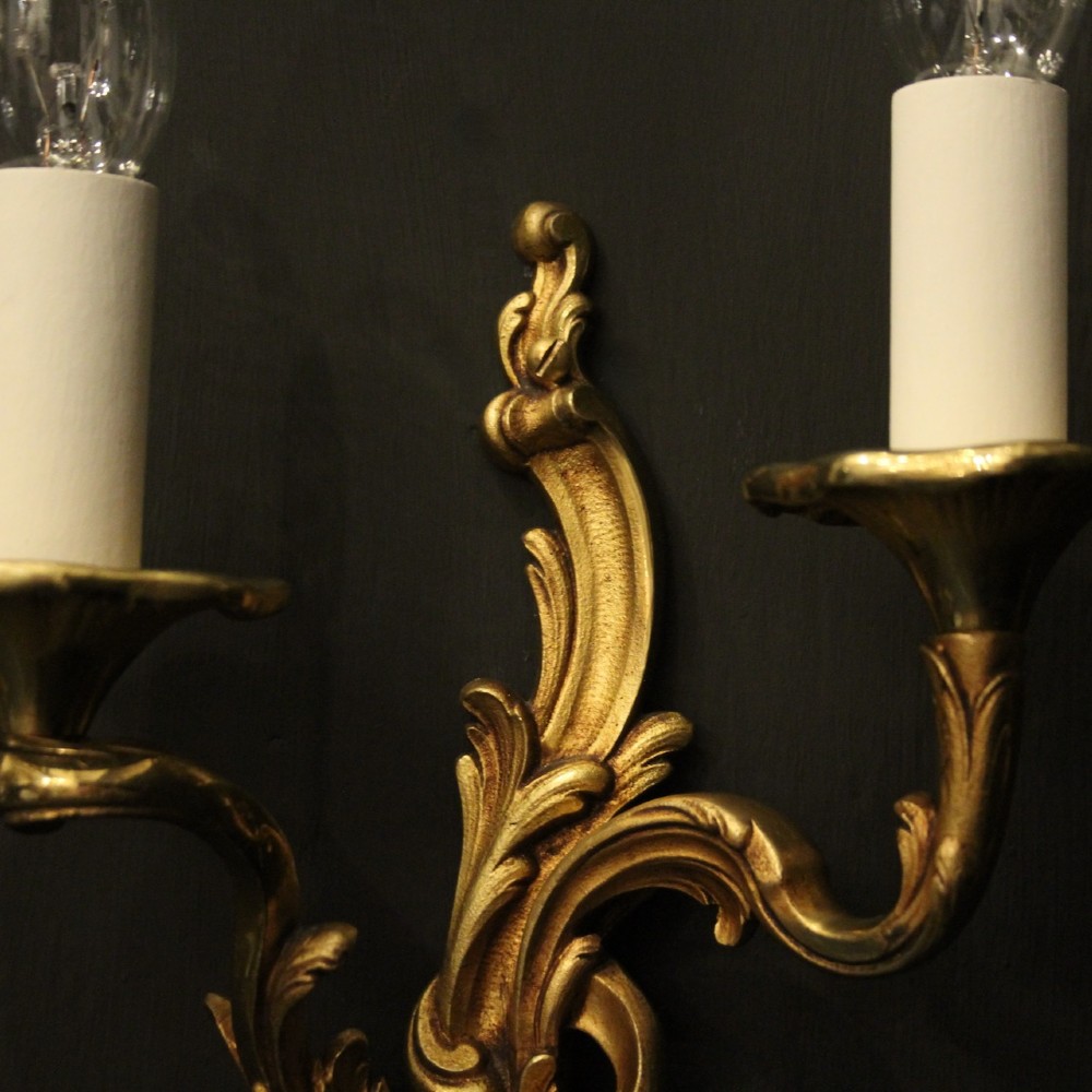 A pair of two-arm French Rococo style gilded bronze wall lights featuring acanthus leaf scrollwork and cream candle holders. View IV