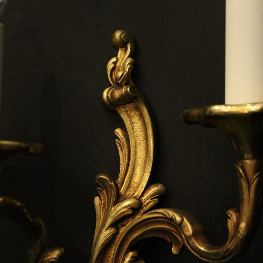 A pair of two-arm French Rococo style gilded bronze wall lights featuring acanthus leaf scrollwork and cream candle holders. View V