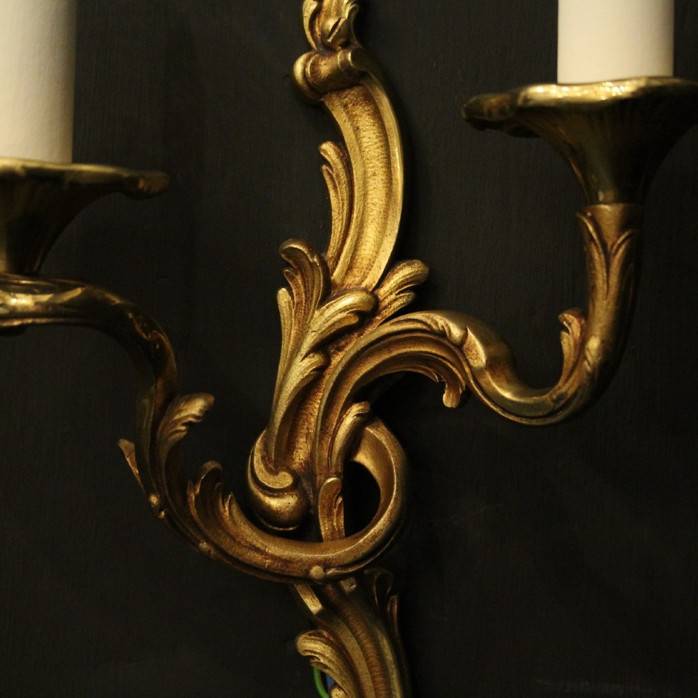A pair of two-arm French Rococo style gilded bronze wall lights featuring acanthus leaf scrollwork and cream candle holders. View VI