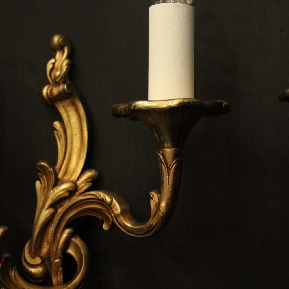 A pair of two-arm French Rococo style gilded bronze wall lights featuring acanthus leaf scrollwork and cream candle holders. View VII