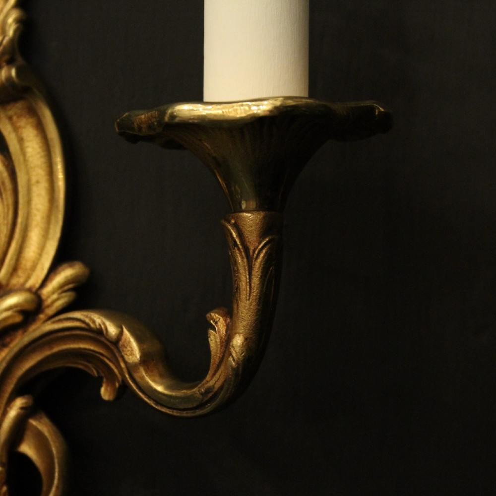 A pair of two-arm French Rococo style gilded bronze wall lights featuring acanthus leaf scrollwork and cream candle holders. View VIII