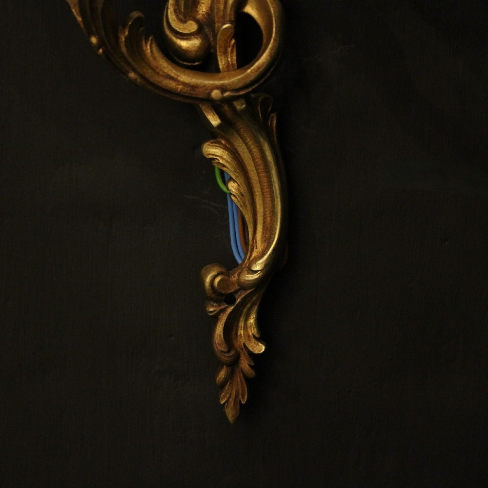 A pair of two-arm French Rococo style gilded bronze wall lights featuring acanthus leaf scrollwork and cream candle holders. View IX