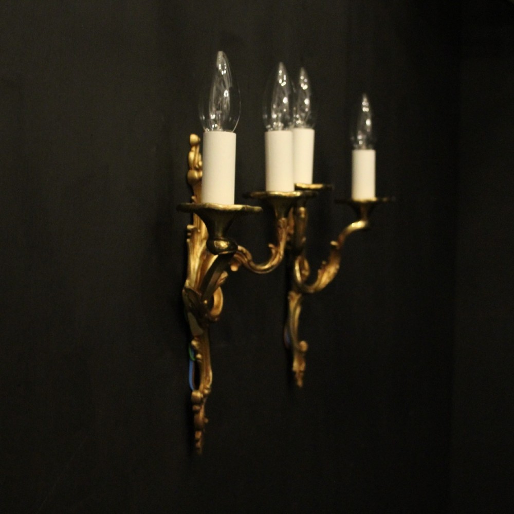 A pair of two-arm French Rococo style gilded bronze wall lights featuring acanthus leaf scrollwork and cream candle holders. View X