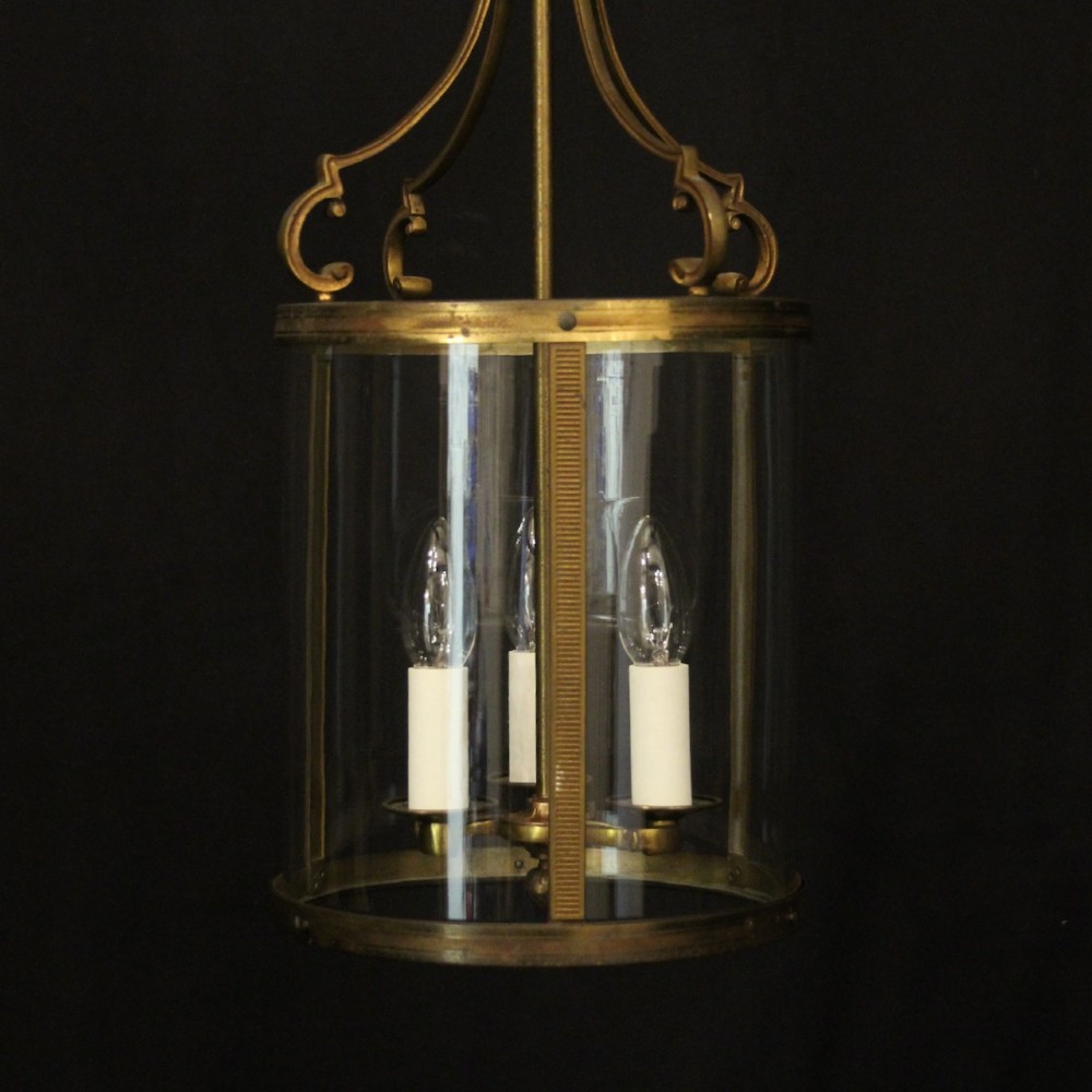 An antique French cylindrical hall lantern featuring a gilded brass frame, curved glass panels, and a three-light interior fitting suspended from a hook. View II