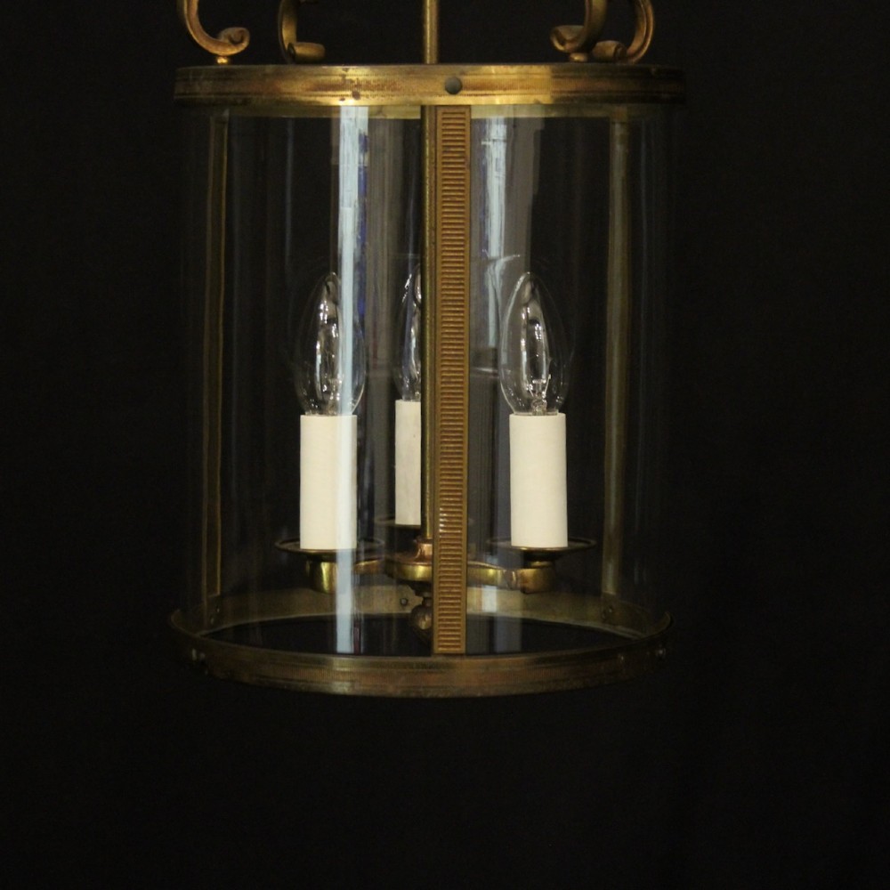 An antique French cylindrical hall lantern featuring a gilded brass frame, curved glass panels, and a three-light interior fitting suspended from a hook. View III