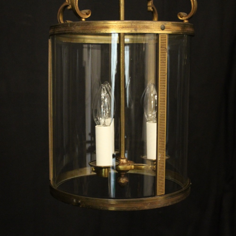 An antique French cylindrical hall lantern featuring a gilded brass frame, curved glass panels, and a three-light interior fitting suspended from a hook. View VIII