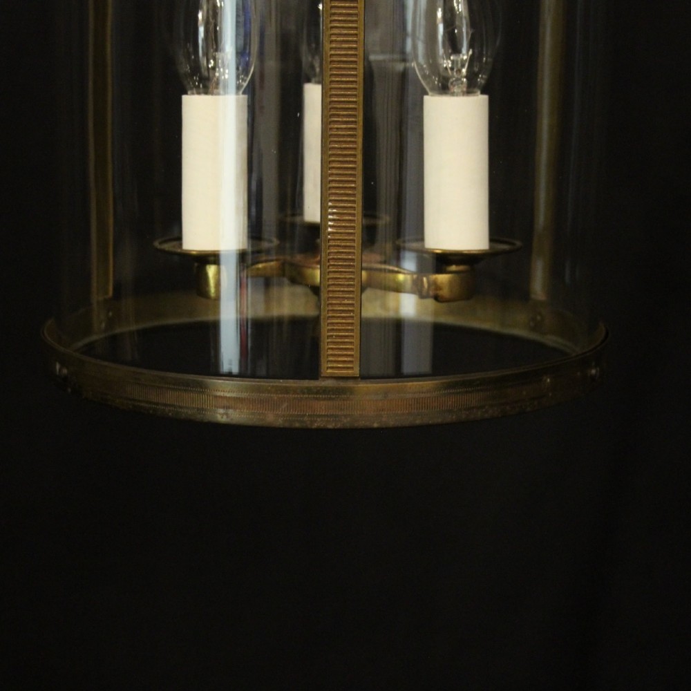 An antique French cylindrical hall lantern featuring a gilded brass frame, curved glass panels, and a three-light interior fitting suspended from a hook. View IX