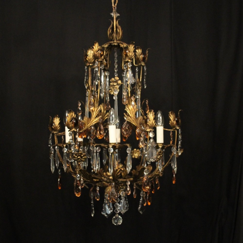 A six-light Florentine chandelier crafted with a gilded leaf metal frame and decorated with suspended clear and amber glass crystal droplets.