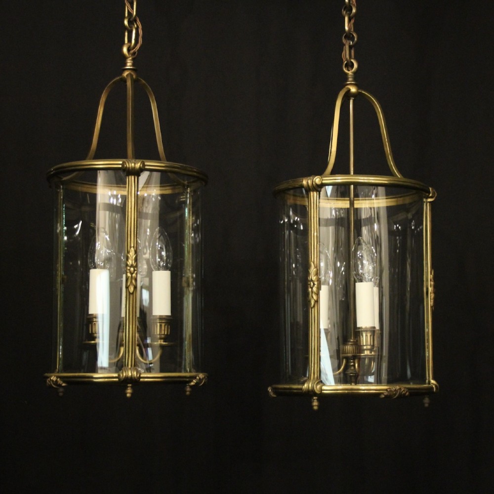 A pair of cylindrical French gilt bronze hanging hall lanterns featuring curved glass panels and internal candle-style light fittings.