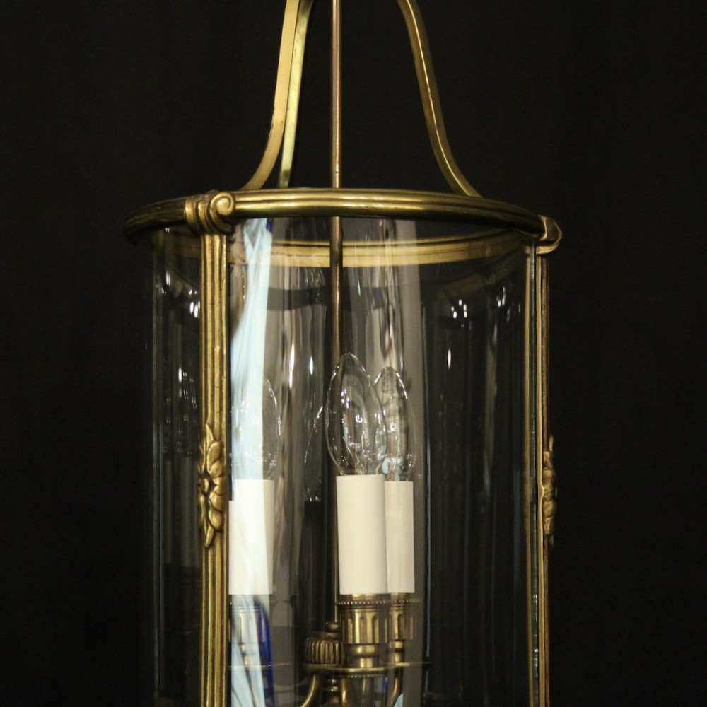A pair of cylindrical French gilt bronze hanging hall lanterns featuring curved glass panels and internal candle-style light fittings. View V