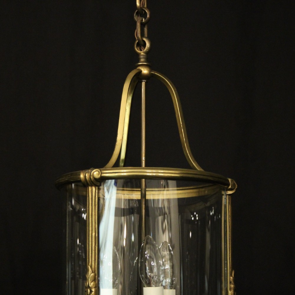 A pair of cylindrical French gilt bronze hanging hall lanterns featuring curved glass panels and internal candle-style light fittings. View VI