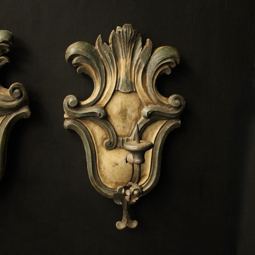 A pair of carved Italian Florentine wall sconces in distressed cream and sage green paint, featuring acanthus crests and single metal candle prickets. View II