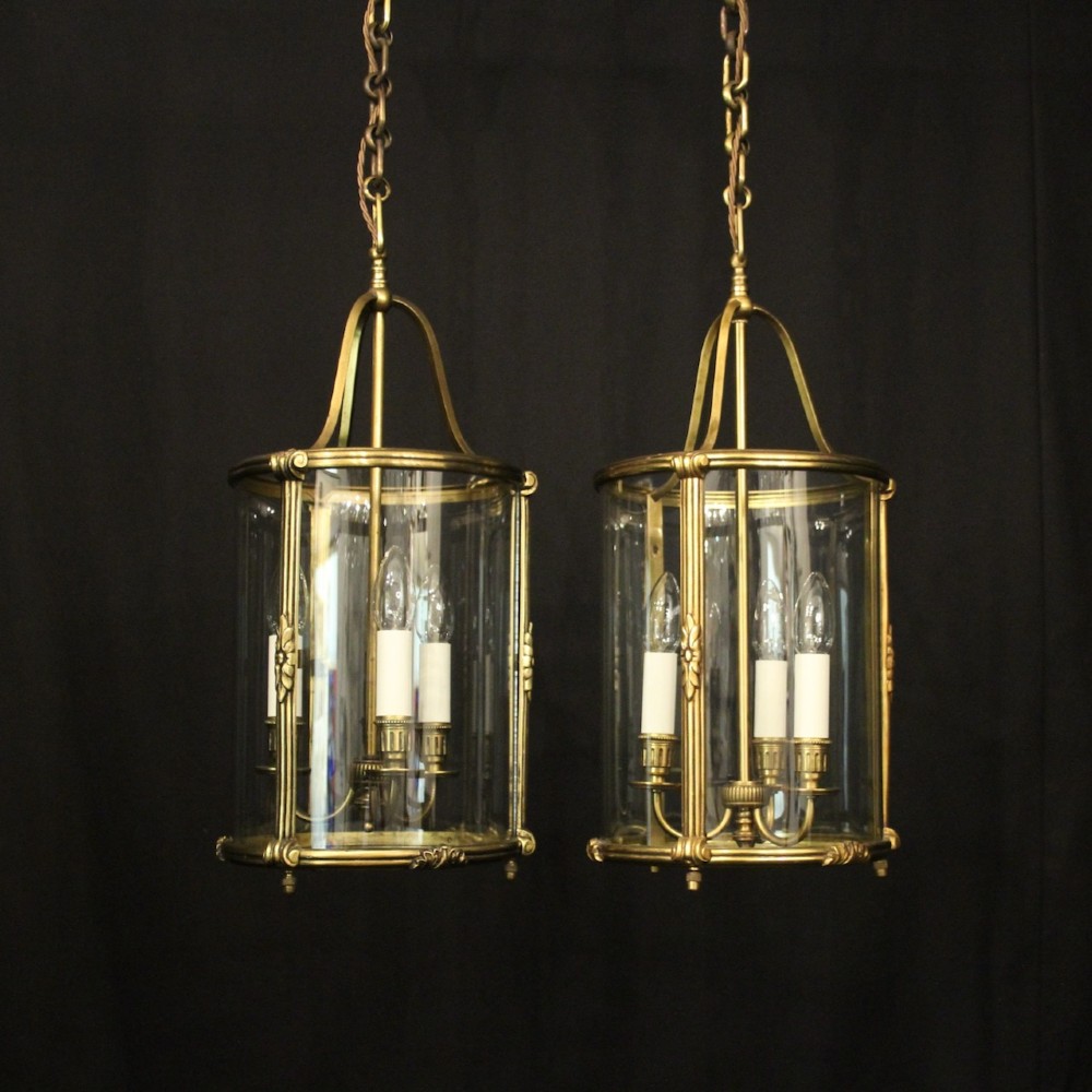 A pair of antique French hall lanterns featuring cylindrical curved glass panels encased in ornate gilded bronze frames with candle-style light fittings.
