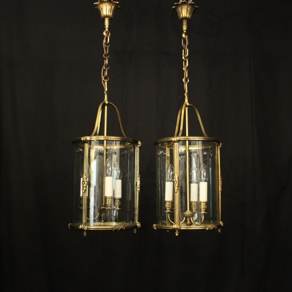 A pair of antique French hall lanterns featuring cylindrical curved glass panels encased in ornate gilded bronze frames with candle-style light fittings. View II