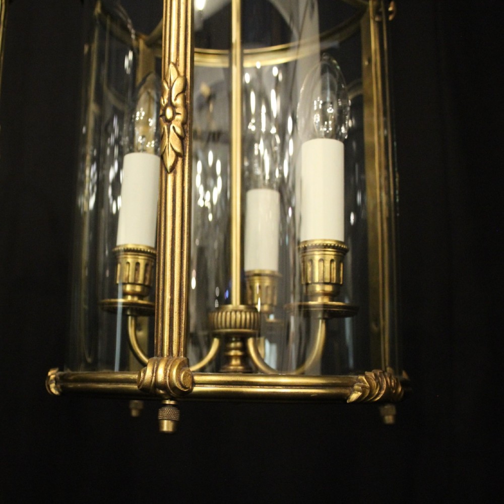 A pair of antique French hall lanterns featuring cylindrical curved glass panels encased in ornate gilded bronze frames with candle-style light fittings. View VII