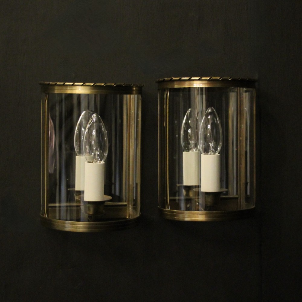A pair of French brass convex half lanterns with curved glass panels and twin candle bulb sockets.